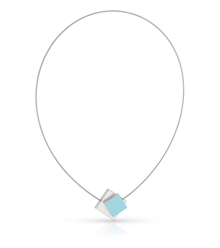 De Collier Vierkant met gekleurd vierkant C263B van CLIC Creations bestaat uit een dunne zilveren draad met daaraan een geometrische hanger met kruisende vormen: een lichtblauwe kubus en een witte kubieke structuur, vastgezet met een magnetische sluiting, afgebeeld op een witte achtergrond.