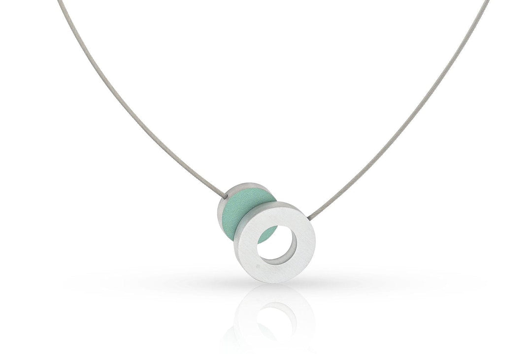 De Collier Gekleurd rondje en een ring C265B van CLIC Creations is een minimalistische ketting met een dunne zilveren ketting, met een ronde hanger met licht mintgroene details. Het heeft een magnetische sluiting voor eenvoudig dragen en is handgemaakt in Nederland, met een elegant, modern design.