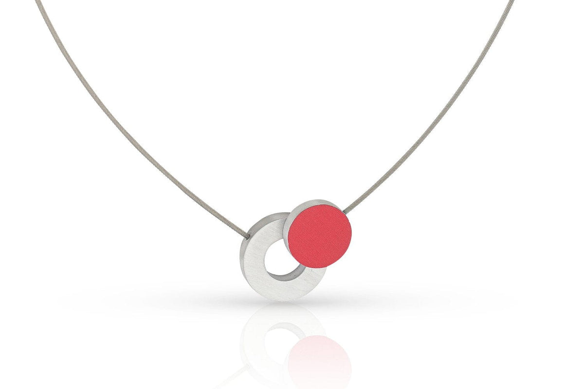 De Collier Gekleurd rondje en een ring C265R van CLIC Creations is een minimalistische ketting met een hanger met ineengestrengelde zilveren en rode cirkels, handgemaakt in Nederland, opgehangen aan een dunne zilveren ketting met een magnetische sluiting voor moeiteloze elegantie.
