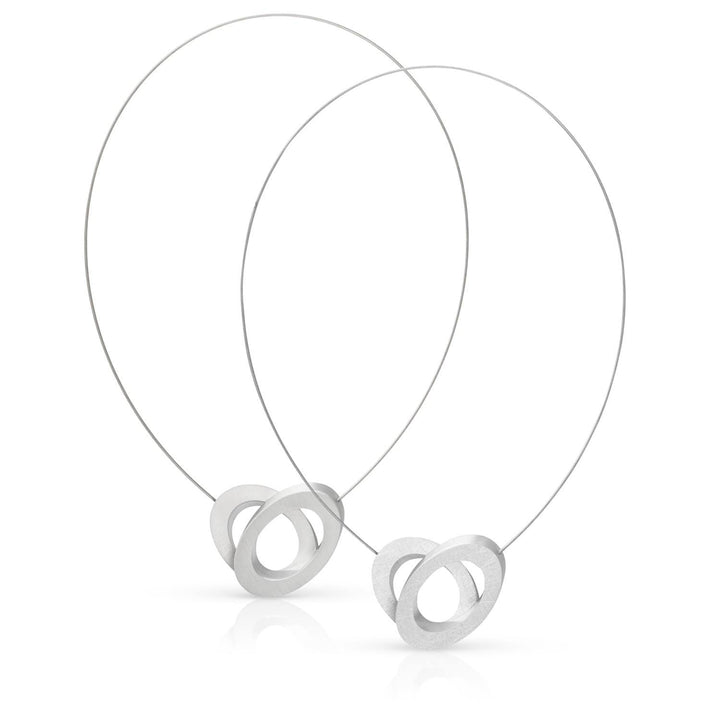 De Collier Ovalen op elkaar C70 van CLIC Creations heeft in elkaar verweven zilveren draadlussen met mat afgewerkte, in elkaar grijpende hartvormige hangers. Deze minimalistische hangers zijn handgemaakt in Nederland en stralen een Uniek design uit. Ze staan rechtop en tonen abstracte artisticiteit.