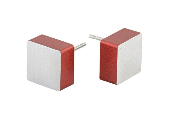De Oorsteker Vierkant Rood O15R van CLIC Creations heeft twee vierkante oordopjes van hypoallergeen chirurgisch roestvrij staal, met een strakke metalen afwerking. Elk heeft een rode zijkant, zilveren voorkant en zichtbare 3,5 mm connectorpin. De oordopjes zijn iets uit elkaar geplaatst en hebben een andere hoek.