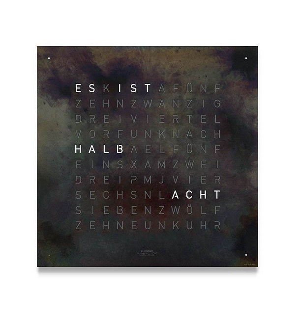 Reloj de pared Qlocktwo Classic en hierro crudo con diseño artístico y letras iluminadas.