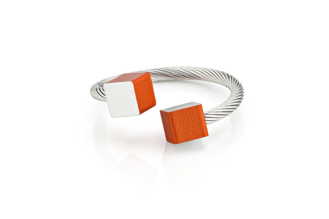 De Ring Kubusjes Oranje R4O van CLIC Creations is een zilveren gedraaide kabelarmband met twee kubusuiteinden: een half zilver, half oranje en de andere helemaal oranje. Het open-top design combineert op unieke wijze eigentijdse stijl met minimalistische flair.