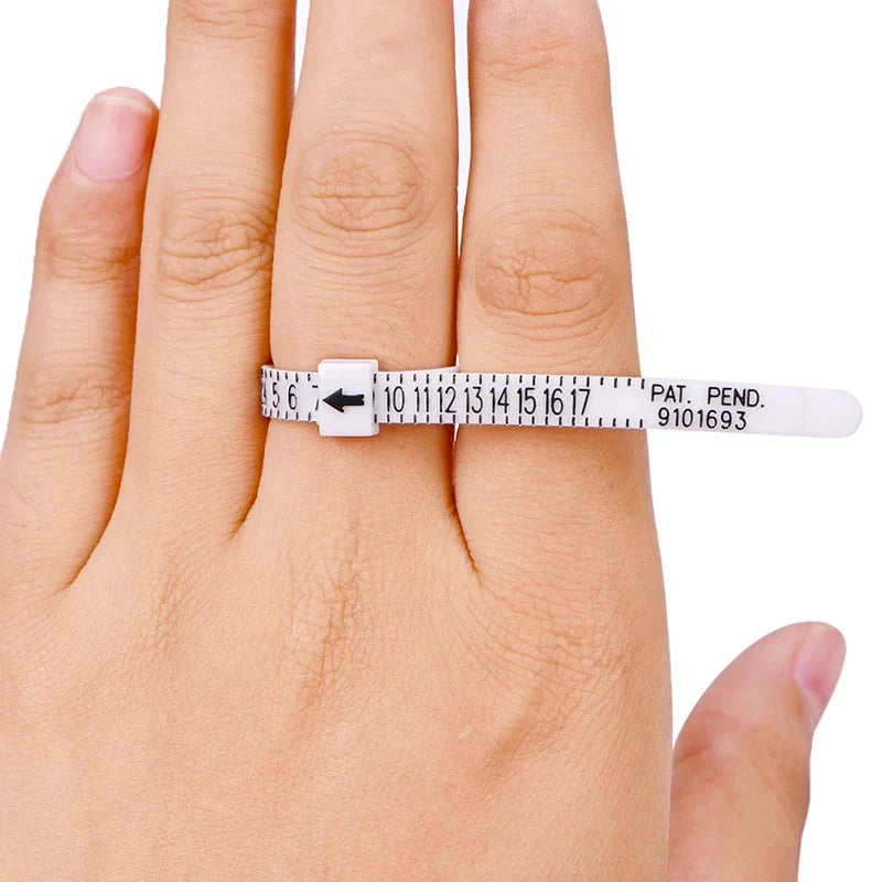 Een hand toont een witte plastic Pas-ring van Juwelier van der Kooij die een vinger omsluit, met zwarte afmetingen, een pijl die de maat aangeeft en getallen van 5 tot 18. Het bevat PAT. PEND. 9101693 voor nauwkeurige maatbepaling om uw perfecte ringmaat te vinden.