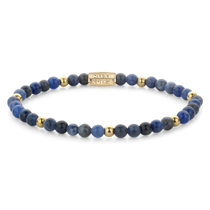 De Rebel & Rose Midnight Blue 4 mm kralenarmband voor dames heeft afwisselend sodaliet edelstenen en gouden kralen, plus een rechthoekige 18 kt geelgouden geïoniseerde bedel gegraveerd met de merknaam.