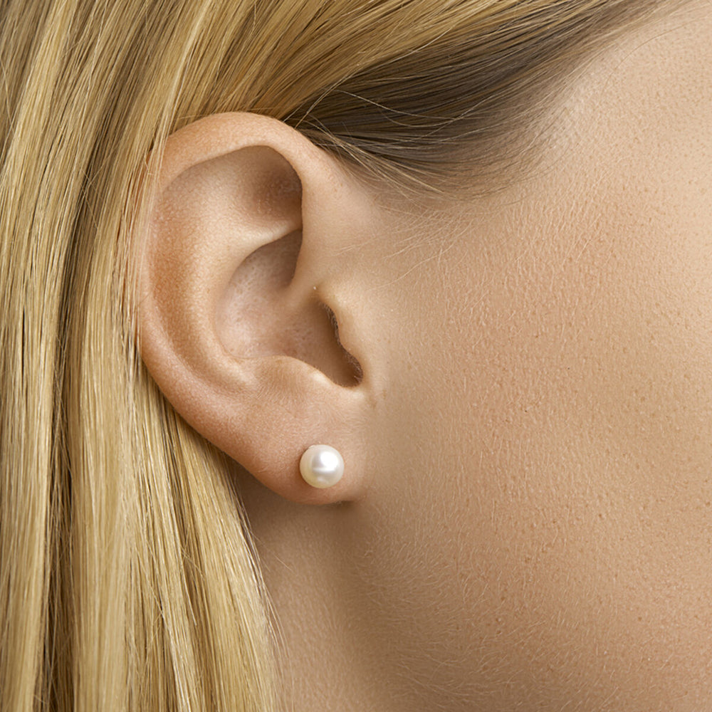 Close-up van een lichtgekleurd persoon met steil blond haar, gekleed in een Van der Kooij Collectie oorknoppen van parelmoer in 14K geelgoud. De achtergrond is neutraal.