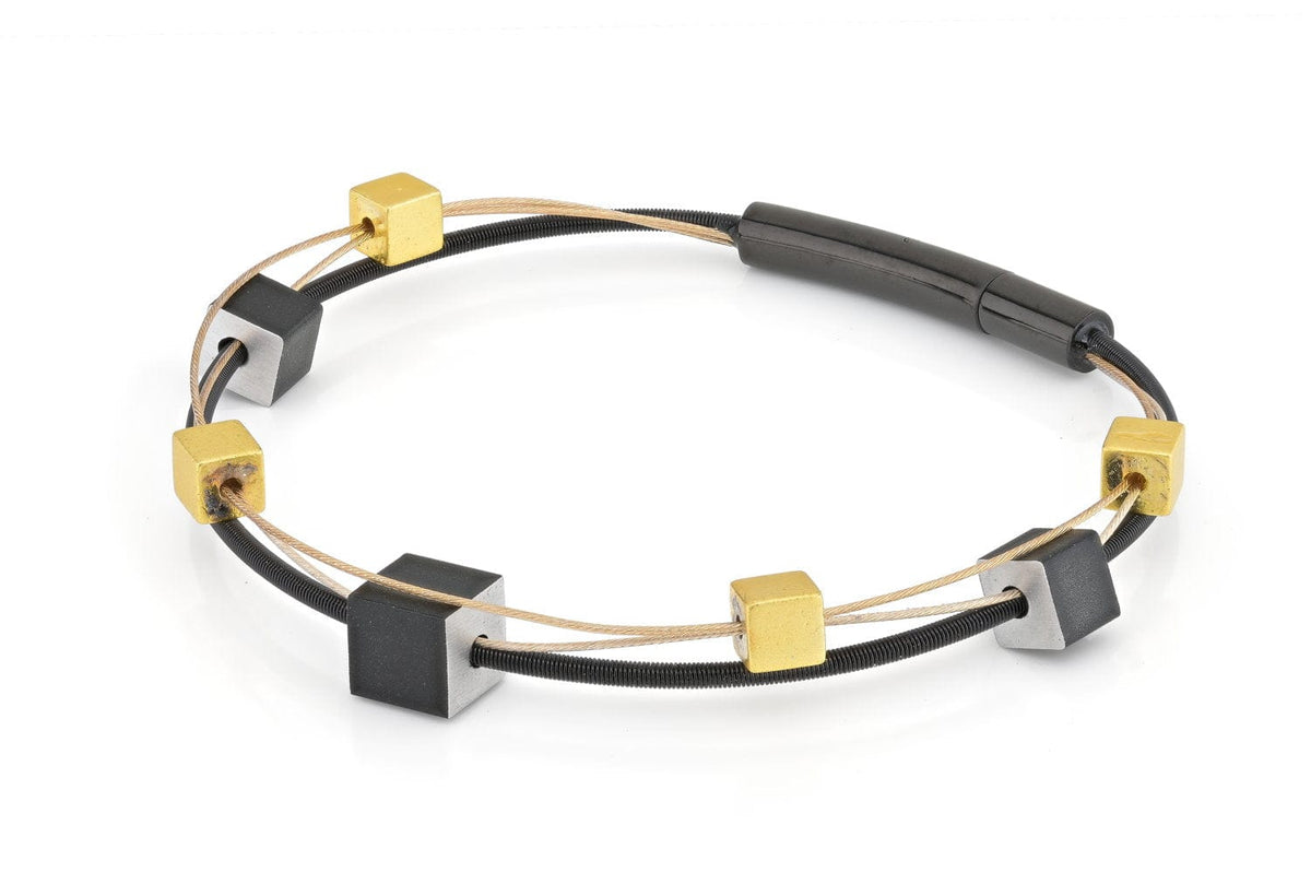 Pulsera con cubos juguetones en color dorado y negro, con detalles en metal y cordón.
