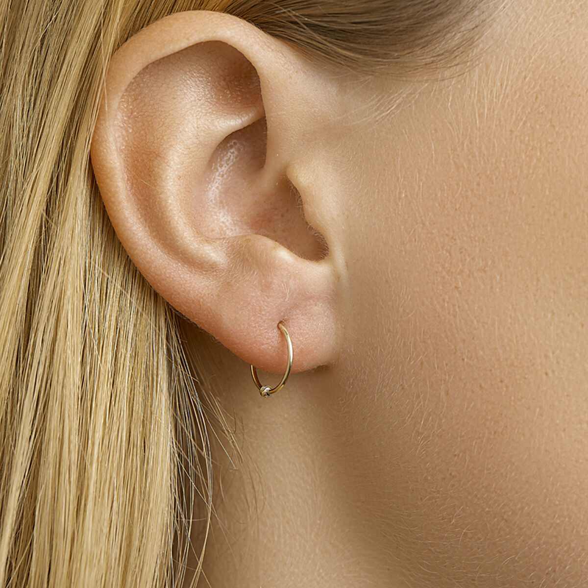Close-up van het oor van een persoon met steil blond haar, met in de oorlel een elegant oorbellen bolletje 14K geelgoud uit de Van der Kooij Collectie.