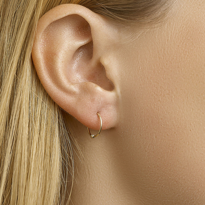 Close-up van het oor van een persoon met steil blond haar, met in de oorlel een elegant oorbellen bolletje 14K geelgoud uit de Van der Kooij Collectie.