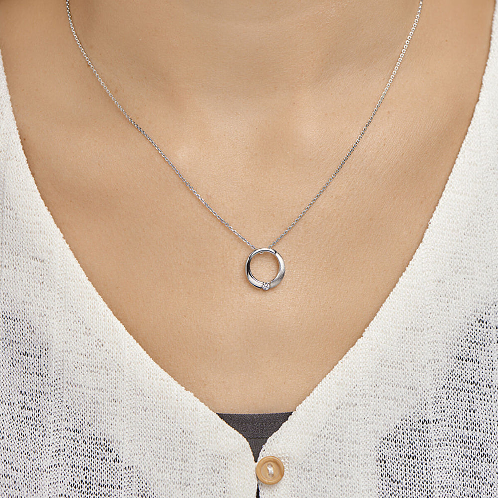 Een close-up van een vrouw met de Van der Kooij Collectie hanger rond zirkonia poli/mat zilver gerhodineerd, voorzien van een ronde hanger met een kleine zirkonia. Ze is gekleed in een wit gebreid topje met één zichtbare knoop.