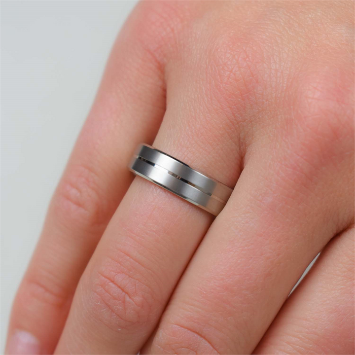 Een close-up van een hand met de Boccia Titanium Ring 0101-22 van Boccia. Deze ring is uitgevoerd in mat titanium en heeft een subtiel groefontwerp. De ringvinger wordt afgebeeld tegen een lichte achtergrond.