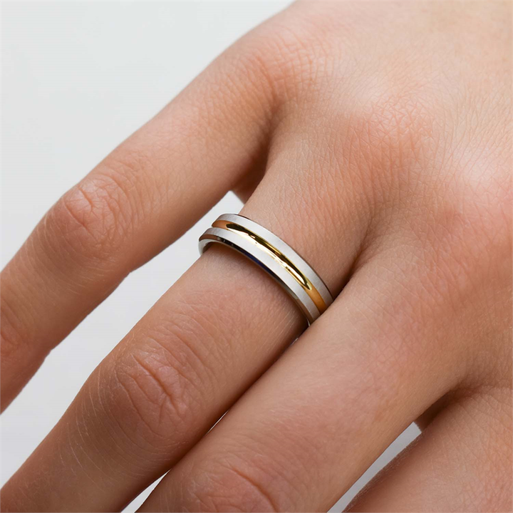 Een close-up van een hand met de Boccia Titanium Ring Bicolor 0144-02 van Boccia. De verweven zilveren en gouden banden op de ringvinger zijn te zien tegen een lichte achtergrond: een tijdloos accessoire.