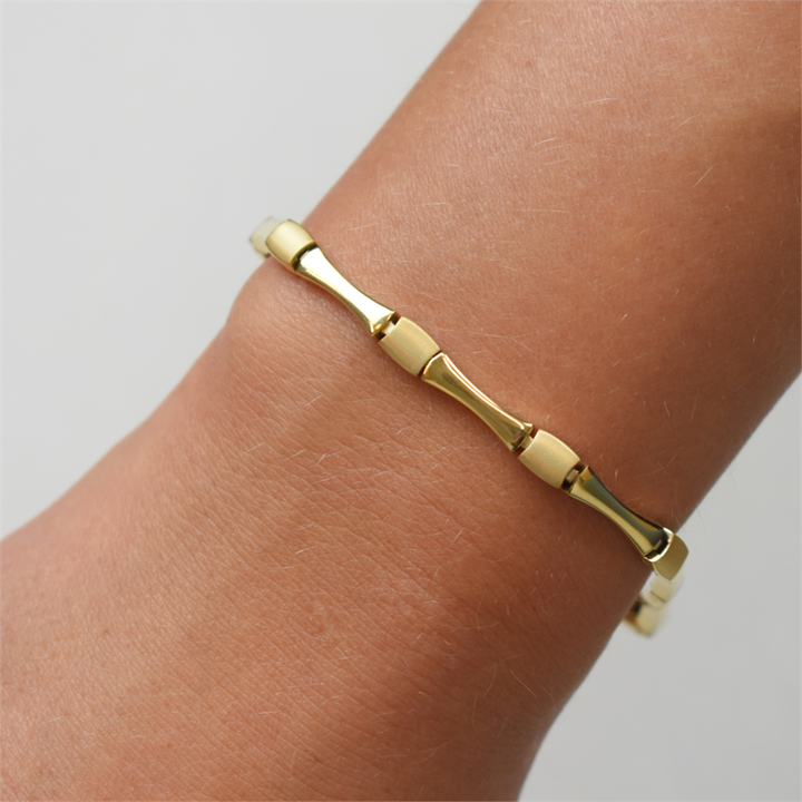 Een close-up van een pols versierd met de Boccia Titanium Armband gp 03037-03, een slanke gouden damesarmband van Boccia met een op bamboe geïnspireerd ontwerp tegen een effen, lichte achtergrond.