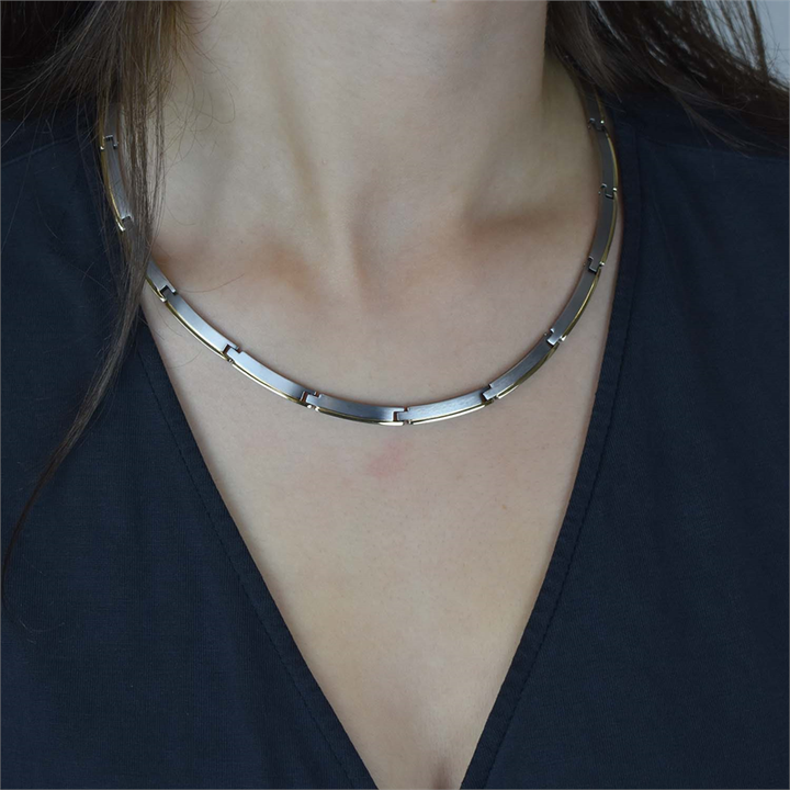 Een close-up van iemand die de Boccia Titanium Collier Bicolor 08028-02 met rechthoekige schakels en een minimalistisch design draagt, gecombineerd met een donkere top met V-hals. Het gezicht van de persoon is niet zichtbaar. Merk: Boccia.