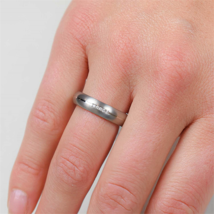 Een close-up van een hand met de Boccia Titanium Ring dia 5/0.025 - 0130-03 van Boccia, met kleine ingelegde diamanten op de ringvinger tegen een lichte, neutrale achtergrond.