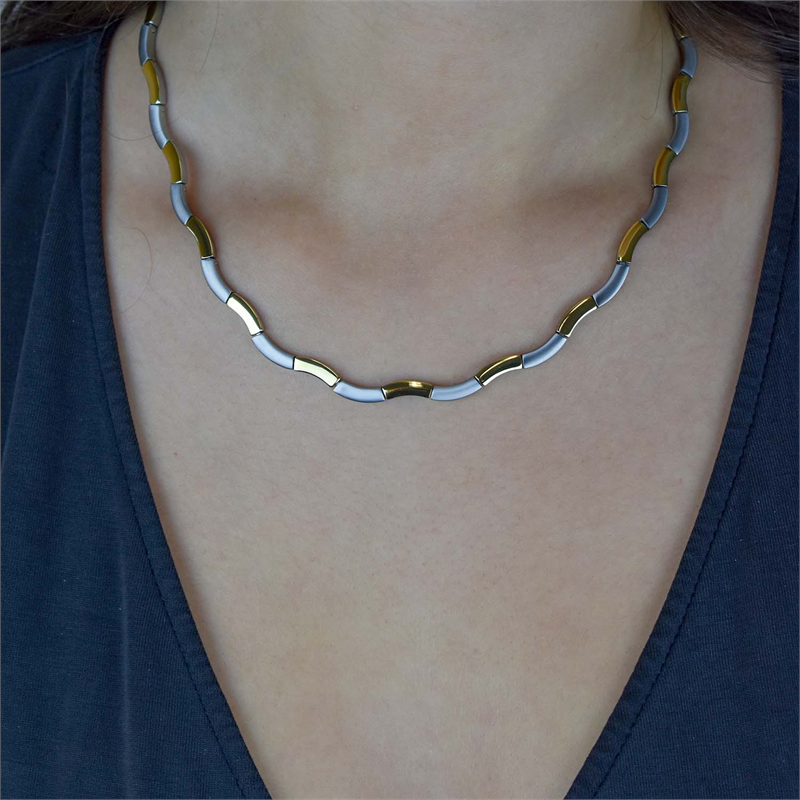 Een persoon draagt de Boccia Titanium Collier Bicolor 0844-02, een stijlvolle titanium ketting met zilveren en gouden segmenten, op een donker V-hals shirt. Het tweekleurige ontwerp volgt sierlijk de halslijn en benadrukt de moderne aantrekkingskracht.