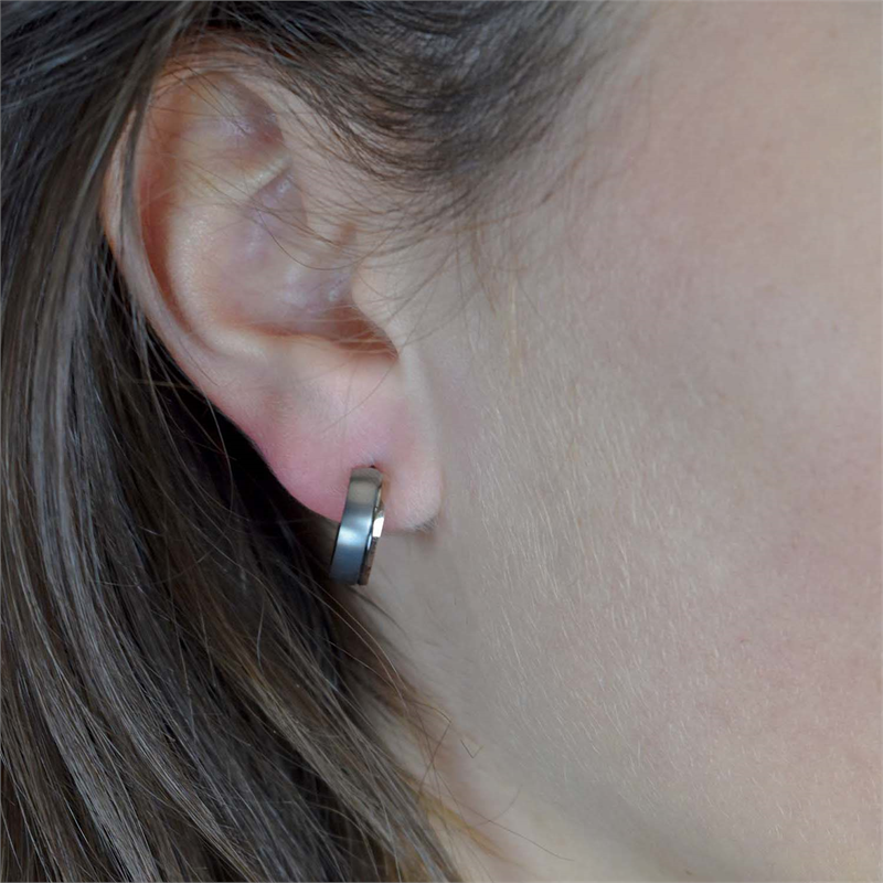 Close-up van het oor van een persoon met steil bruin haar, die Boccia Titanium Oorringen Bicolor rgp 0539-16 draagt. De kleine zilveren en rosé vergulde oorring van Boccia zit in de oorlel tegen een lichte huid en een neutrale achtergrond.