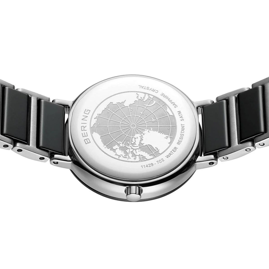 De achterkant van de Bering dames horloge zwarte wijzerplaat - 11429-702 toont een gegraveerde wereldkaart, BERING en WATER RESISTANT tekst, een zilver-zwarte metalen band en is voorzien van duurzaam saffierglas voor extra krasbestendigheid.