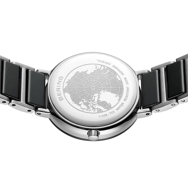 De achterkant van de Bering dames horloge zwarte wijzerplaat - 11429-702 toont een gegraveerde wereldkaart, BERING en WATER RESISTANT tekst, een zilver-zwarte metalen band en is voorzien van duurzaam saffierglas voor extra krasbestendigheid.
