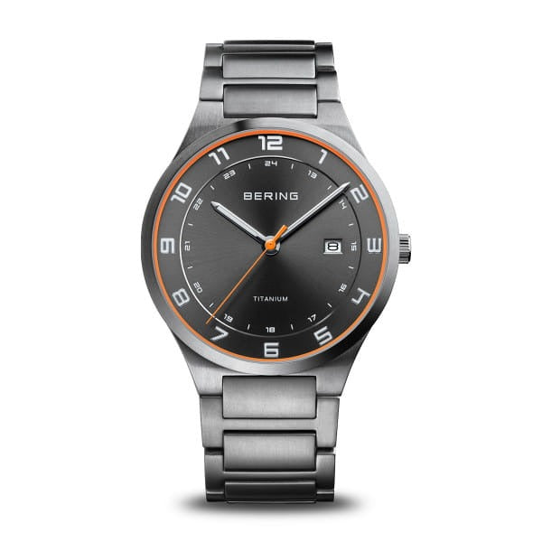 Reloj de titanio con esfera negra, detalles en naranja y correa de eslabones metálicos.