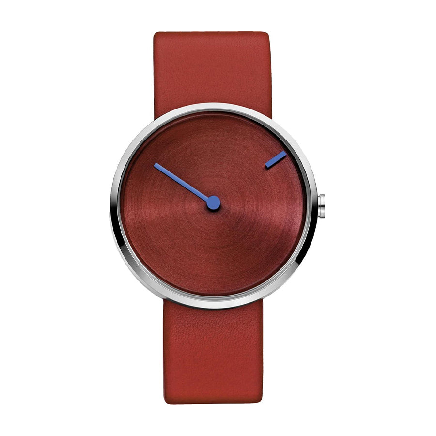 Reloj con esfera roja y correa de cuero marrón, manecillas azules y diseño minimalista.