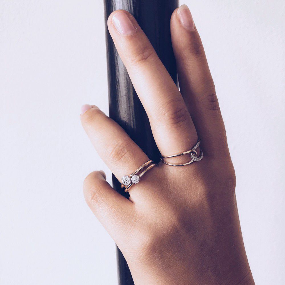 Een gemanicuurde hand houdt een zwarte paal vast en draagt twee ringen: één is de 14 karaats bicolor gouden damesring met briljant geslepen diamanten van Excellent Jewelry, beide fonkelend tegen een effen, lichte achtergrond.