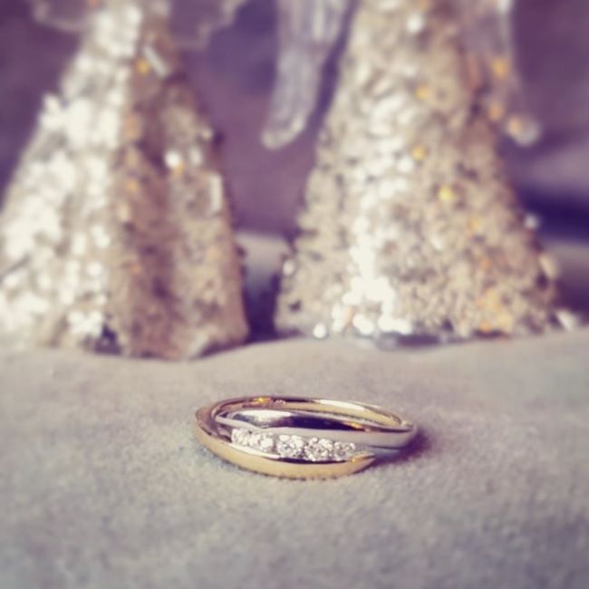 De 14K Bicolor Geel- en Witgouden Damesring met 0,16 ct Briljant Diamant van Excellent Jewelry ligt op een zacht oppervlak, met twee vaag glinsterende kegelvormige decoraties op de achtergrond.