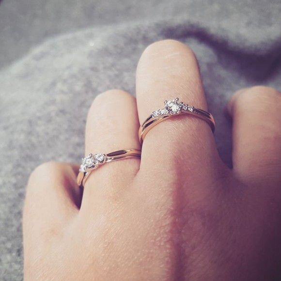 Een close-up van een hand met twee Elegante Bicolor Damesringen met Briljant Diamant (0.22 crt) van Excellent Jewelry, met sprankelende diamanten op de wijs- en middelvinger, tegen een zachte grijze achtergrond.