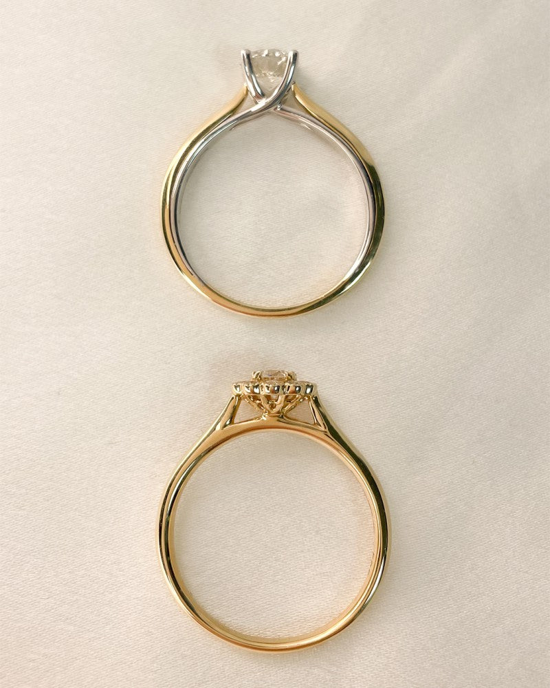 Twee 14k tweekleurige geel- en witgouden ringen van Excellent Jewelry, elk bezet met een 0,74ct H/SI-1 briljantdiamant, worden getoond op crèmekleurige stof - de ene van bovenaf gezien in een prongzetting, de andere van opzij gezien met elegante ontwerpdetails.