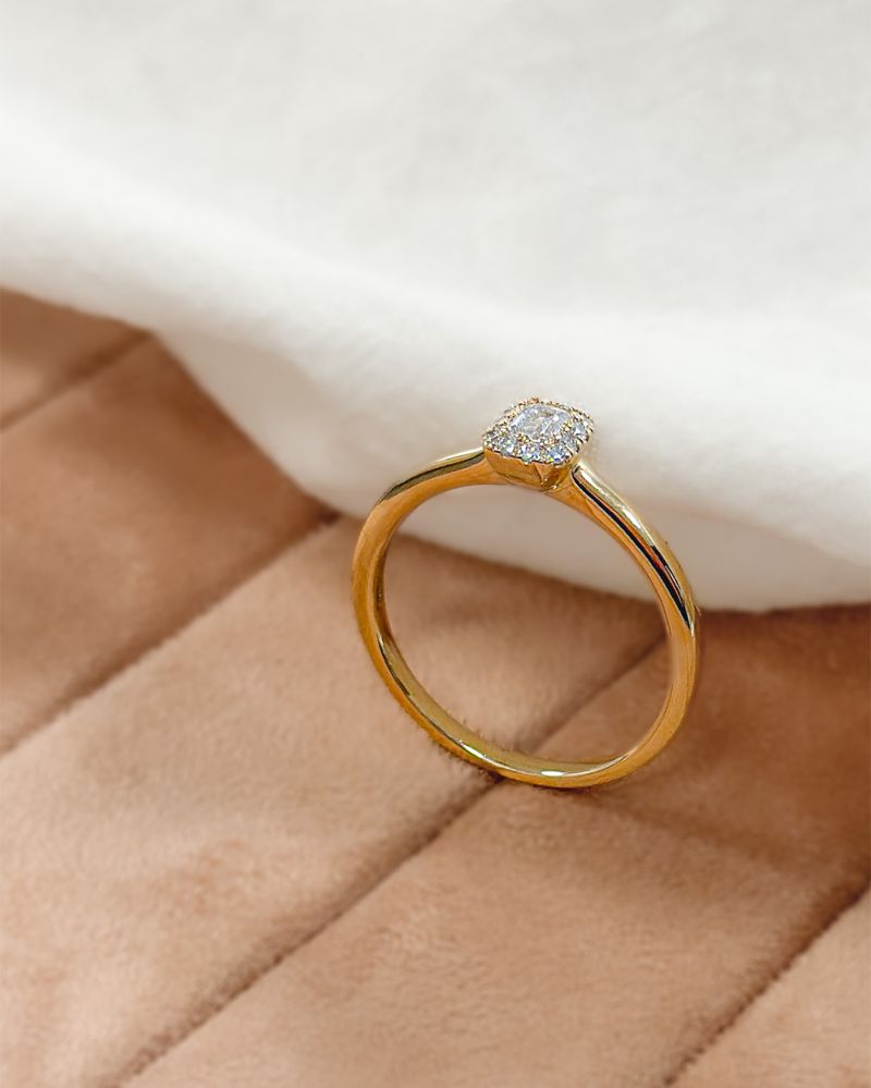 De Verfijnde Geelgouden Ring met Baguette Diamant 0.24 crt. van Excellent Jewelry ligt op een zachte, beige, gewatteerde ondergrond naast een wit, donzig stofje.