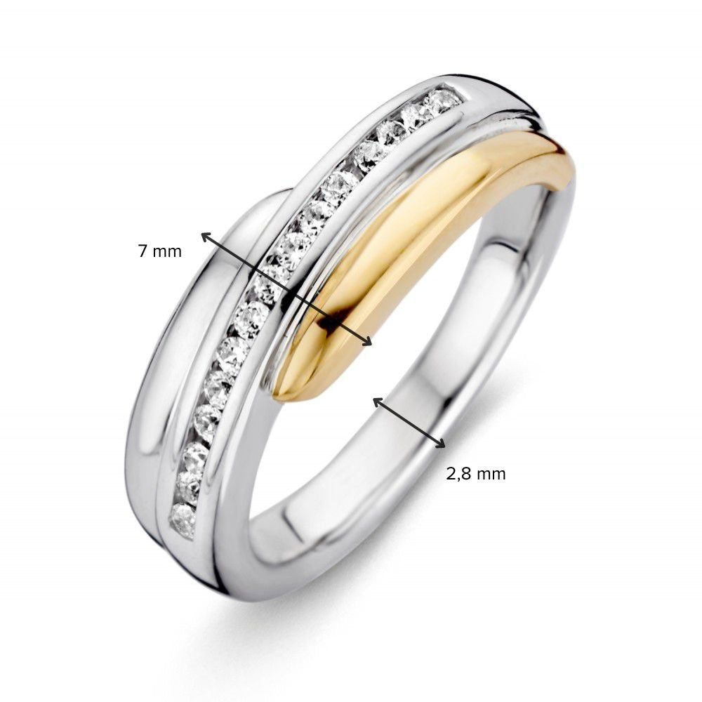 De Excellent Jewelry Zilveren Damesring met 14 Karaat Geel Gouden Zetting en Witte Zirkonia heeft een tweekleurige band van zilver en goud, bezet met witte zirkonia. Boven is de ring 7 mm breed, onderaan 2,8 mm.