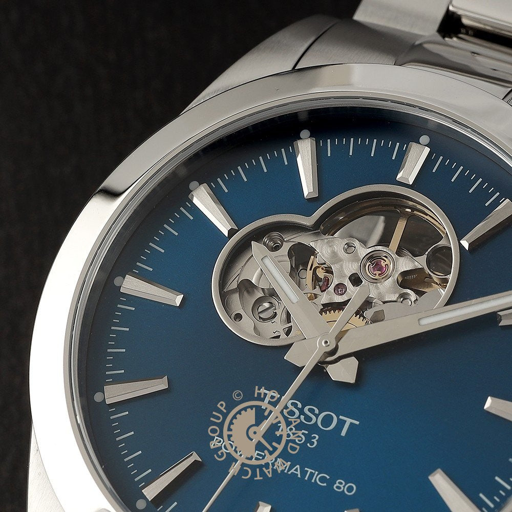 Close-up van het Tissot Gentleman Powermatic 80 Open Heart polshorloge van Tissot, met een blauwe wijzerplaat, zilveren uurmarkeringen en een open hart uitsnede op 12 uur die het Powermatic 80 uurwerk laat zien.