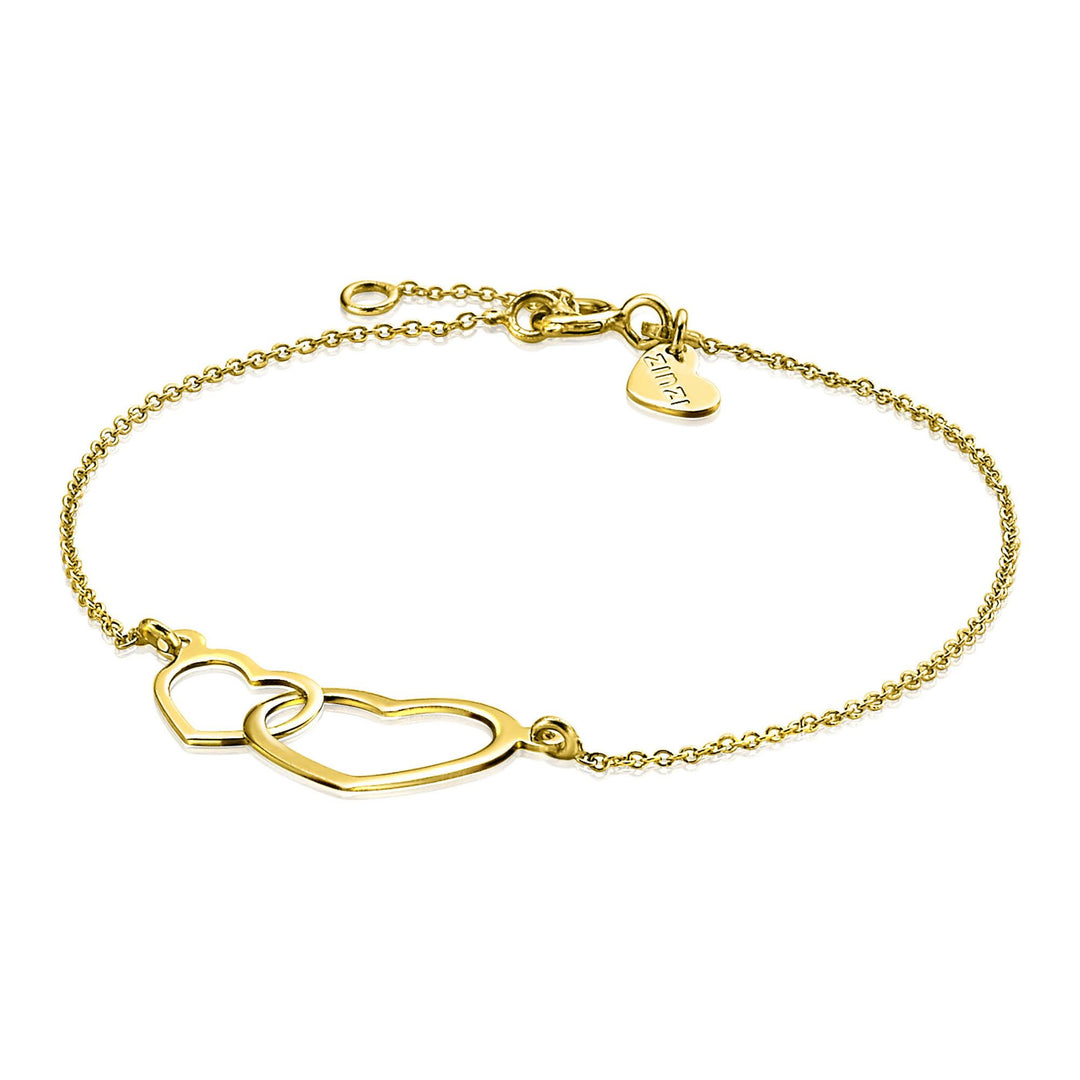 De Zinzi Armband Goud Zga114 heeft twee in elkaar grijpende hartvormen die met elkaar verbonden zijn door een dunne jasseronketting en een verstelbare sluiting met een klein hangertje voor extra elegantie.